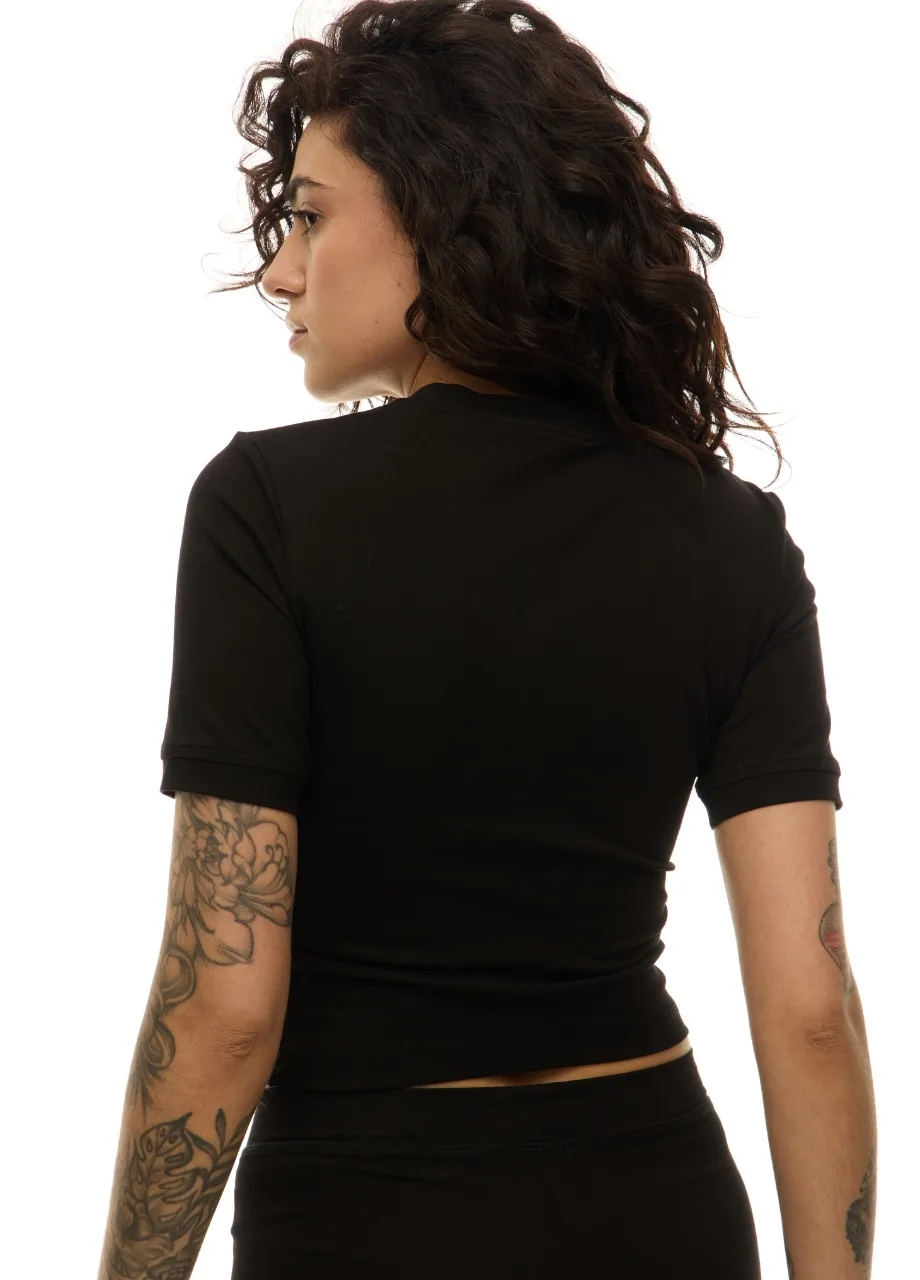 3 › Str/Cd Wear Profile view of a woman with curly dark hair wearing a black short-sleeve top, tattoos visible on her arms, seen from the back/side.