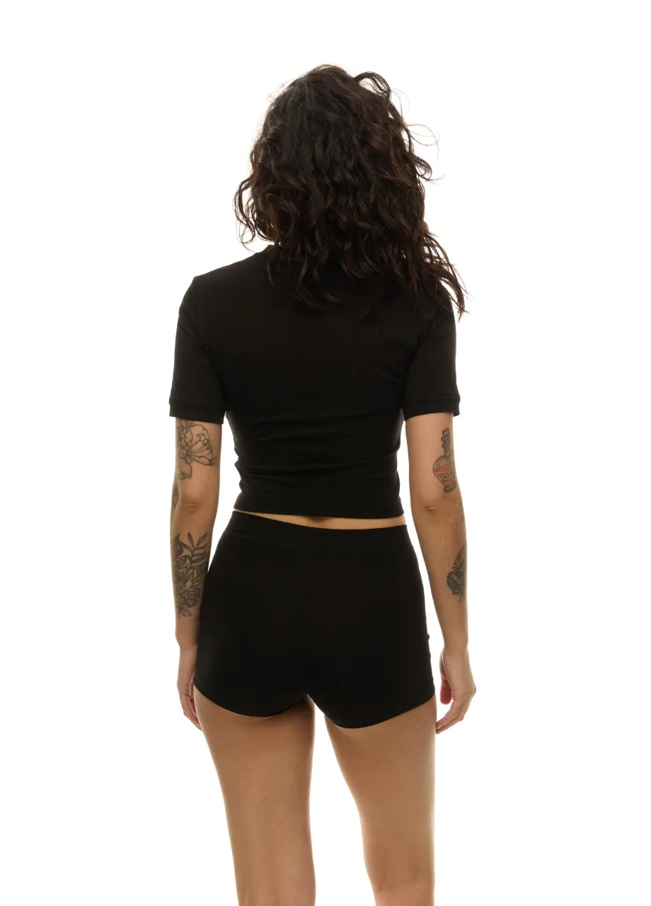 4 › Str/Cd Wear Person standing with back to camera, wearing a black cropped top and black shorts; tattoos on both arms are visible.