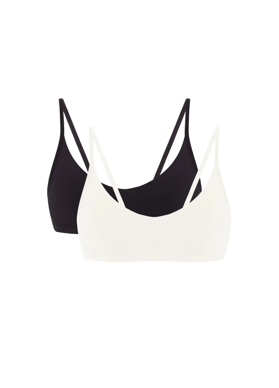 9 › Str/Cd Wear Two bralettes, one white and one black, layered with thin straps visible against a white background.