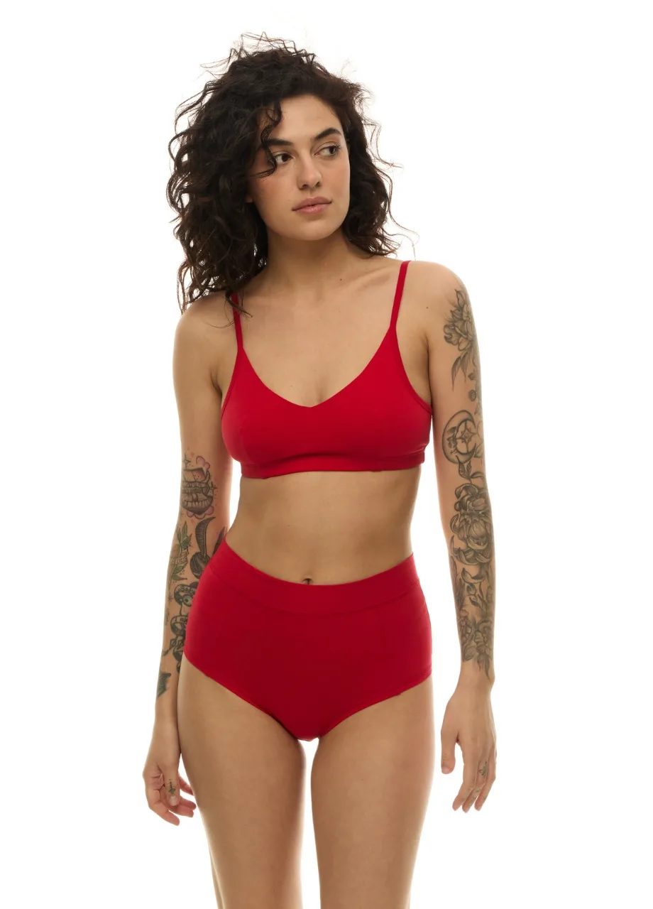 WP611217 › Str/Cd Wear Woman modeling a red lingerie set (bralette and high-waisted briefs) with tattoos on both arms, standing against a white background.