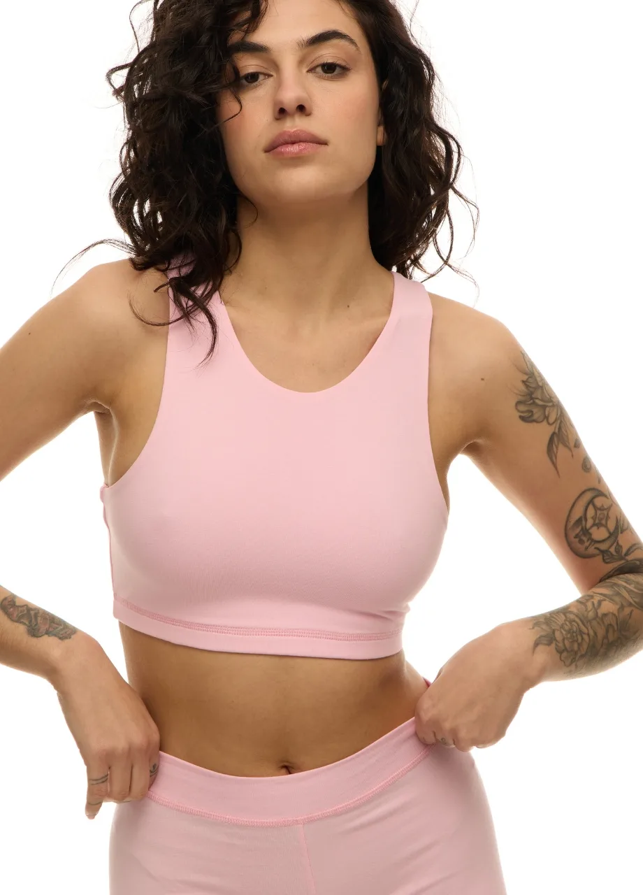 WS509510 › Str/Cd Wear Woman with dark wavy hair wearing a light pink sports bra and matching leggings, hands on hips, tattoos on arms.