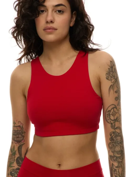 Woman in a red athletic crop top with tattoos on both arms and a neutral expression against a white background.