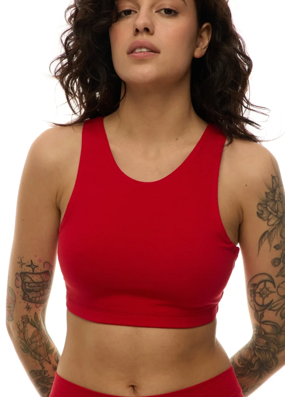 WS509515 › Str/Cd Wear Woman facing forward in a red athletic crop top; visible tattoos on both arms and a neutral expression