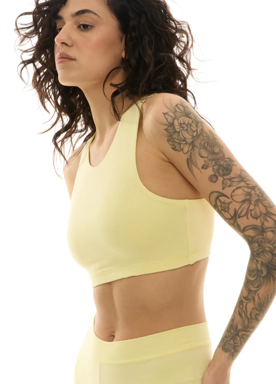 WS509518 › Str/Cd Wear Side profile of a woman in a pale yellow sports bra and leggings, with a floral tattoo sleeve on her right arm.