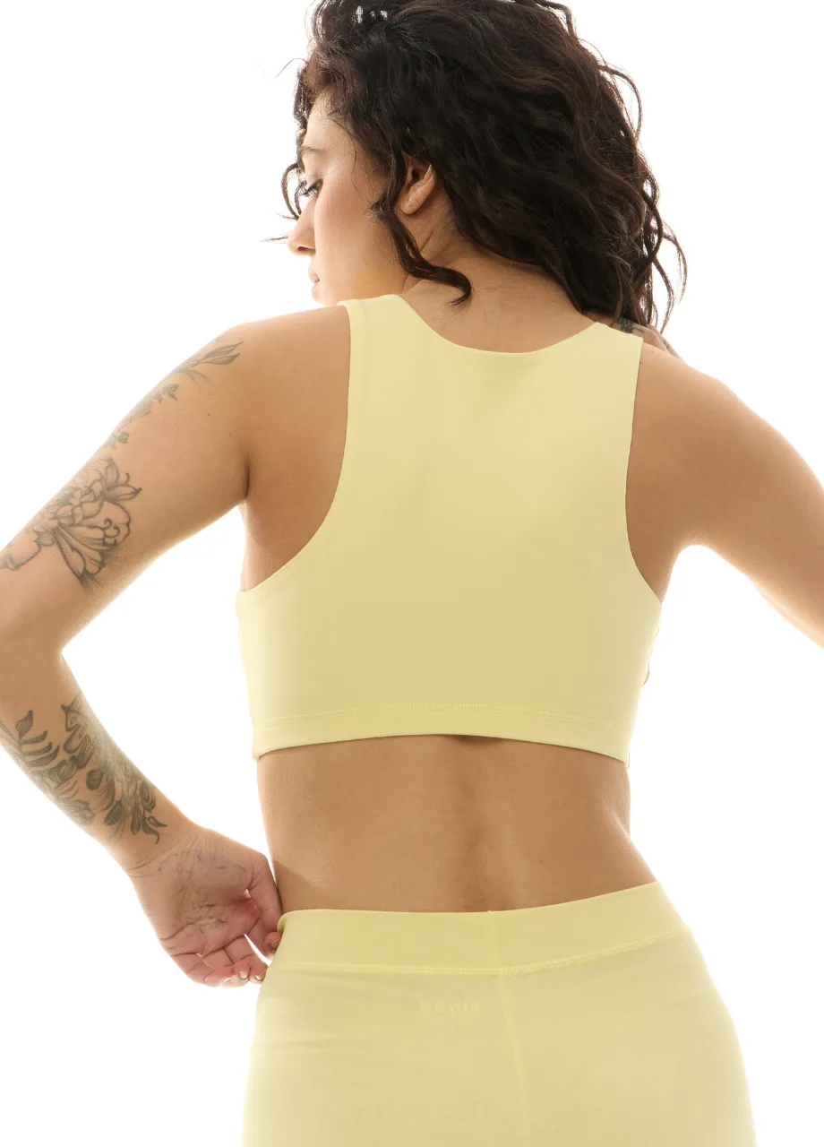 WS509519 › Str/Cd Wear Back view of a tattooed woman in pale yellow athletic set (sports bra and leggings), with hands on hips.