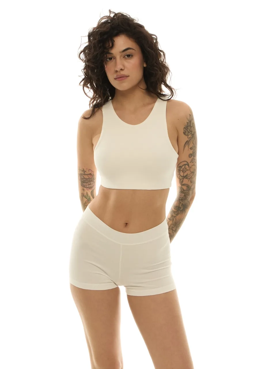 WS50955 › Str/Cd Wear Woman with curly hair in a cream sports bra and matching high-waisted shorts; visible arm tattoos.