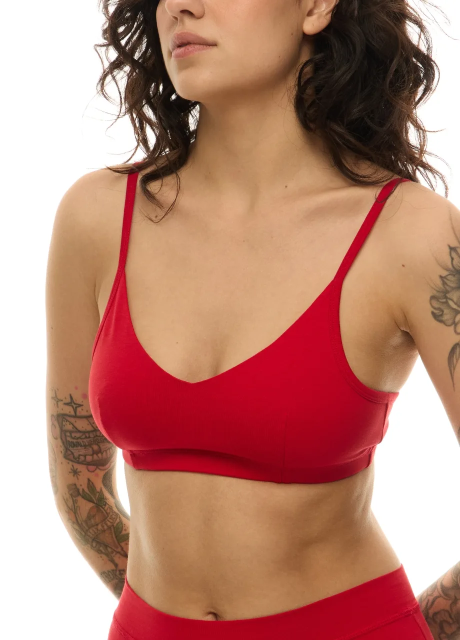WS511114 › Str/Cd Wear Torso shot of a woman wearing a red bra with thin straps; tattoos appear on both arms and she has a neutral expression.