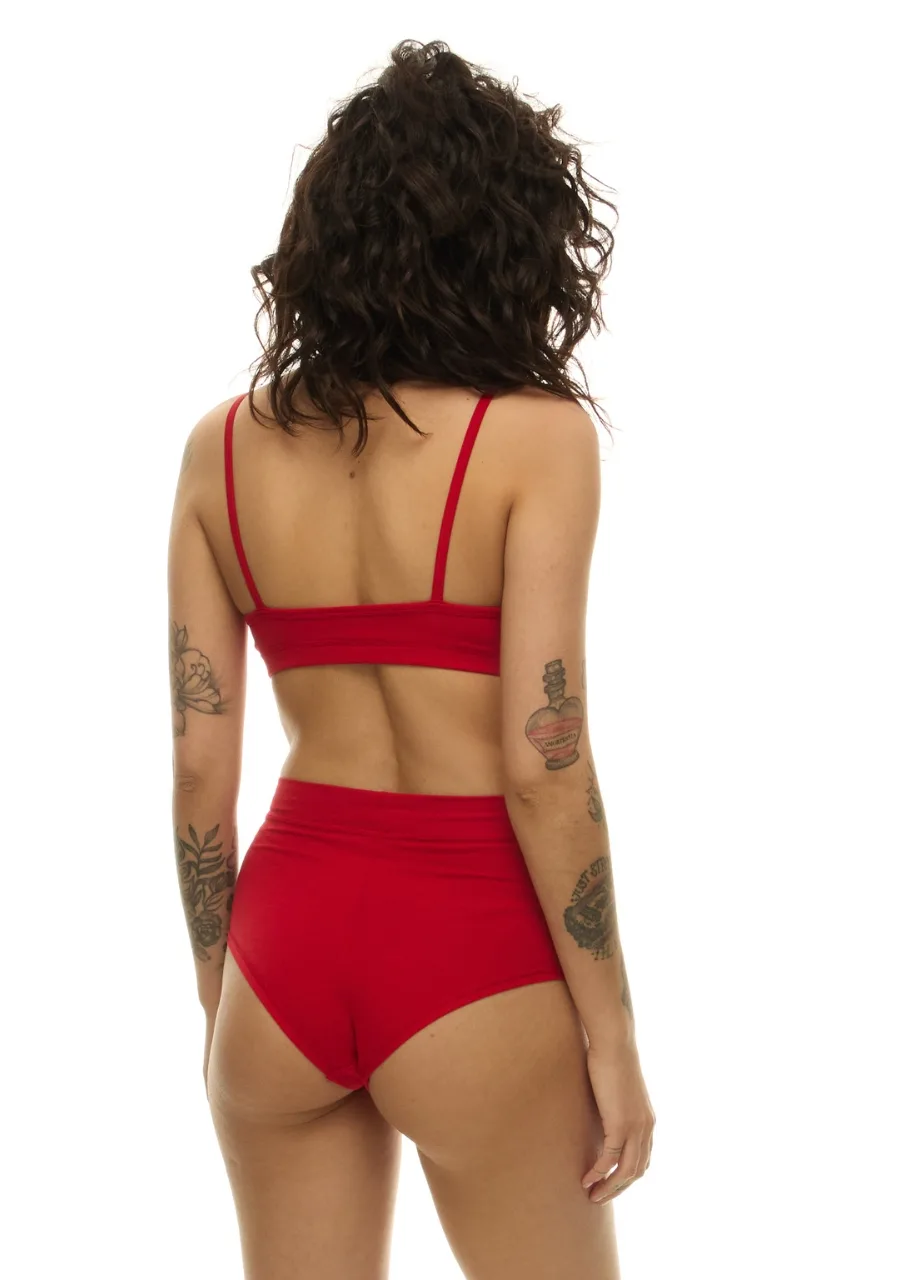 WS511116 › Str/Cd Wear Woman seen from behind wearing a red bralette and high-waisted briefs; curly dark hair and tattoos on both arms are visible.