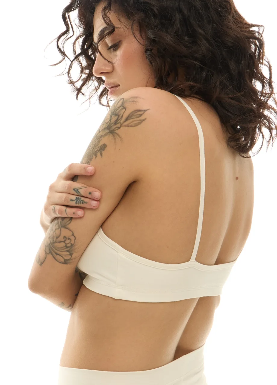 WS51112 › Str/Cd Wear Woman wearing a cream/brassiere top, shown from the back with a floral tattoo on her upper arm and curly dark hair.