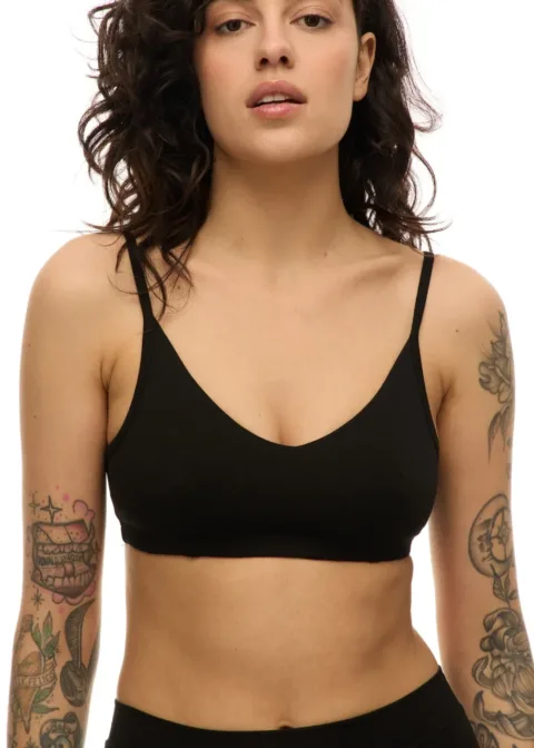 WS51115 Close-up of a woman wearing a black bralette, showing tattoos on both arms, against a white background.