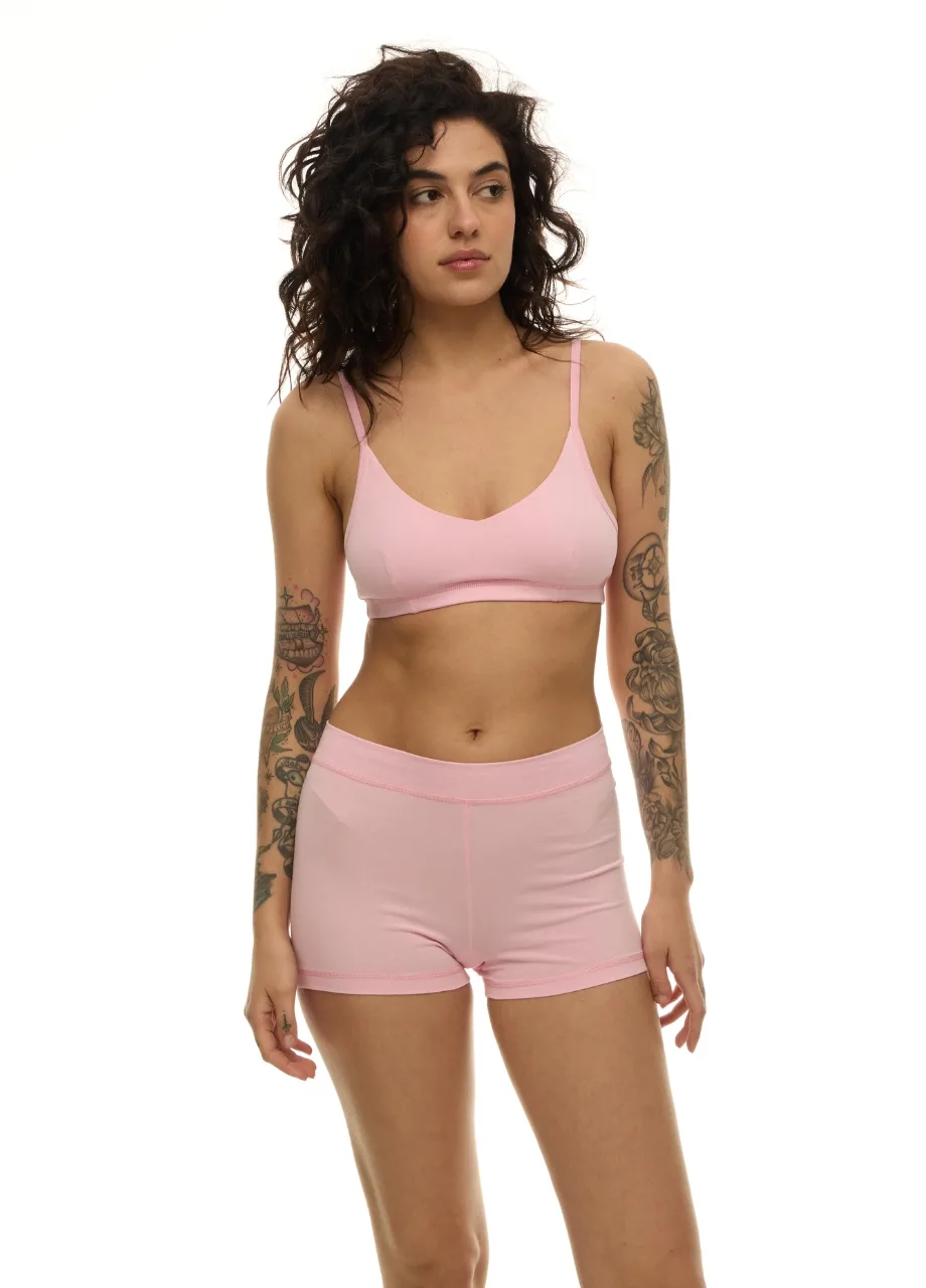 WU1313013 › Str/Cd Wear Woman in a light pink bra and matching shorts lingerie set, standing with arms relaxed, visible arm tattoos