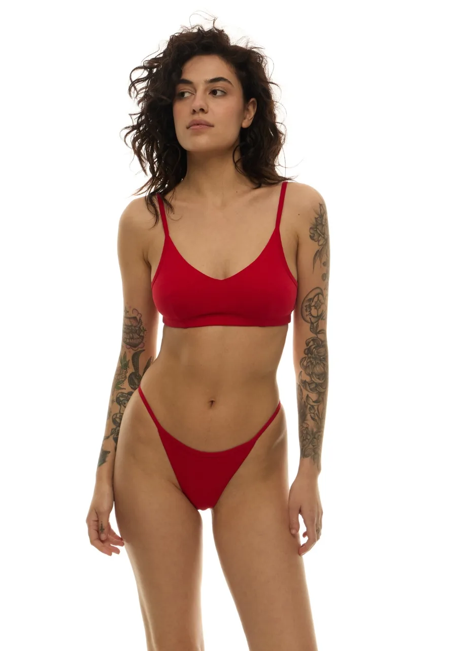 WU1314118 › Str/Cd Wear Woman with curly dark hair wearing a red bikini, standing against a white background with tattoos on both arms.