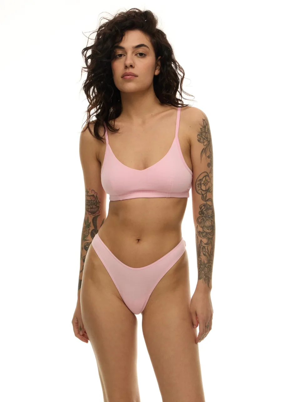 WU1314313 › Str/Cd Wear Woman standing in a light pink bra and thong lingerie set, facing forward with arms relaxed, visible tattoos on arms.