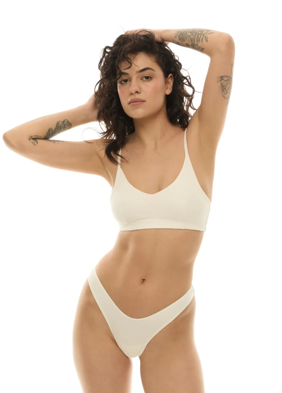 WU131434 › Str/Cd Wear Model in a cream bra and matching high-cut briefs, arms raised behind the head against a white background.