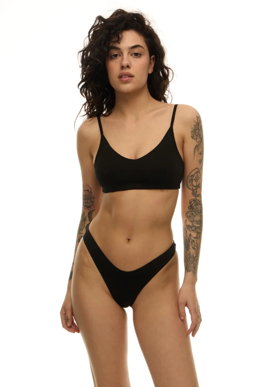 WU131438 › Str/Cd Wear Woman wearing a black bikini with a triangle top and high-cut bottoms, standing against a white studio backdrop.