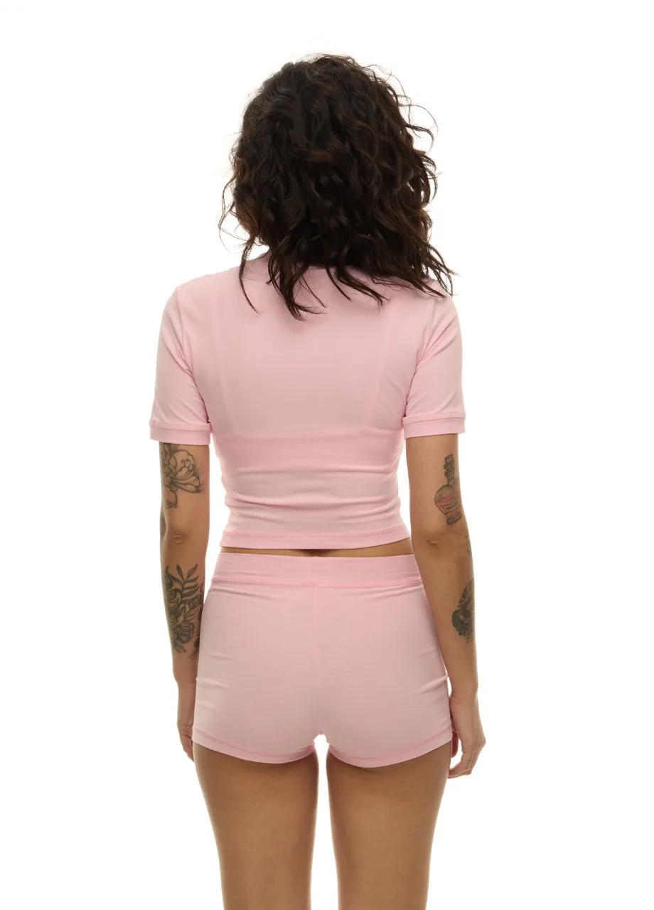 22 › Str/Cd Wear Back view of a person wearing a light pink cropped T-shirt and matching shorts; dark curly hair, visible arm tattoos.