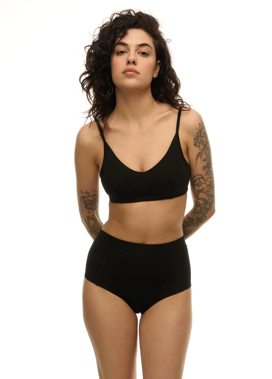 2 › Str/Cd Wear Model wearing black bra and high-waisted underwear, standing with arms behind back, showing tattoos on both arms against a white background.