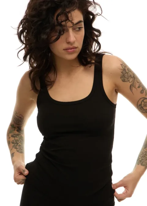 Woman with dark wavy hair in a black tank top, looking to the side as she adjusts the garment.