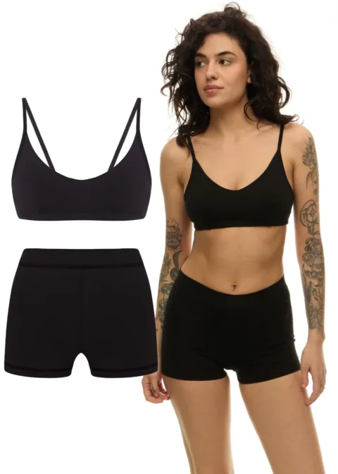 Model wearing a black bralette-style sports bra and matching black seamless shorts; product set shown with separate top and bottom.