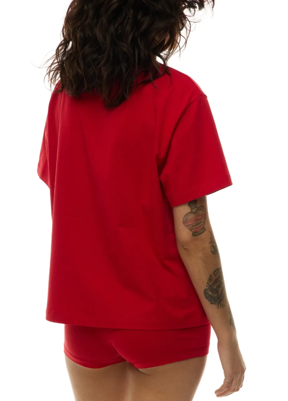 53 › Str/Cd Wear Person with curly dark hair wearing a red short-sleeve shirt and matching red shorts, viewed from behind, with tattoos on the forearm visible.