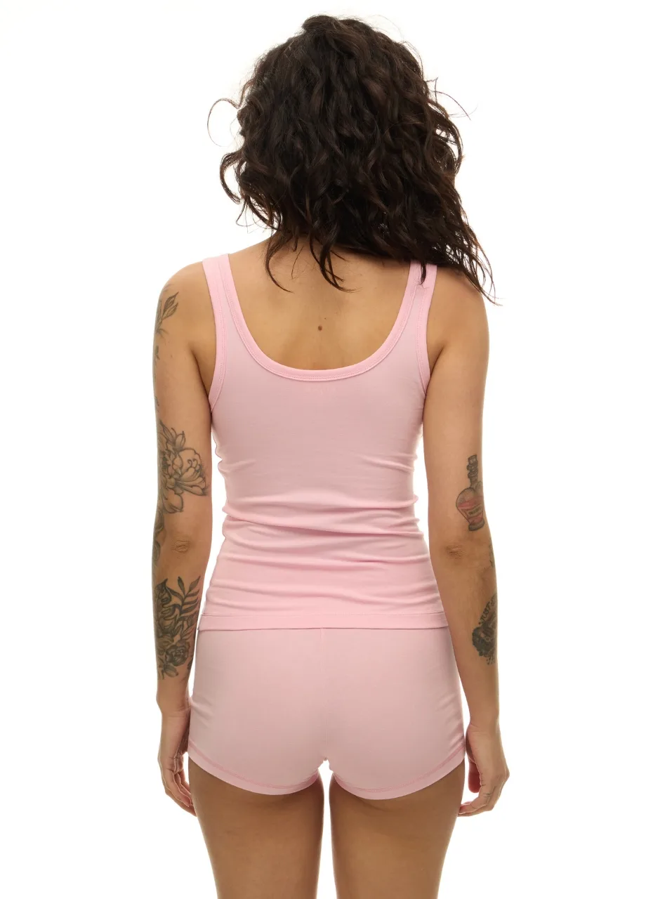 61 › Str/Cd Wear Woman with curly dark hair viewed from behind, wearing a light pink tank top and matching shorts; tattoos are visible on both arms.