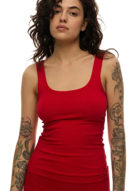 Woman with wavy dark hair wearing a red fitted tank top, tattoos visible on both arms.