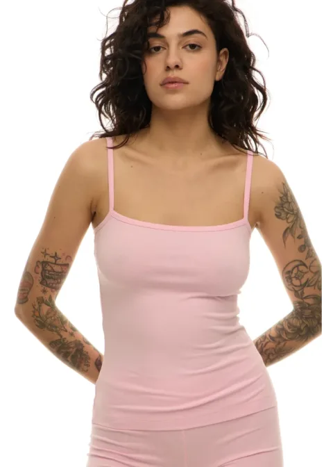 Front view of a woman with dark wavy hair wearing a light pink spaghetti-strap tank top; visible tattoos on both arms.