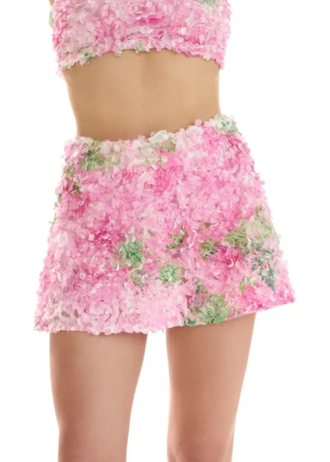 Person wearing a pink petal-covered crop top and matching mini skirt against a white background.