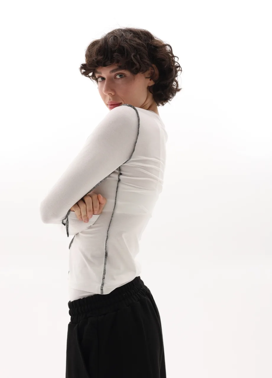 13 › Str/Cd Wear Person in profile with arms crossed, wearing a white long-sleeve top and black pants against a white background.