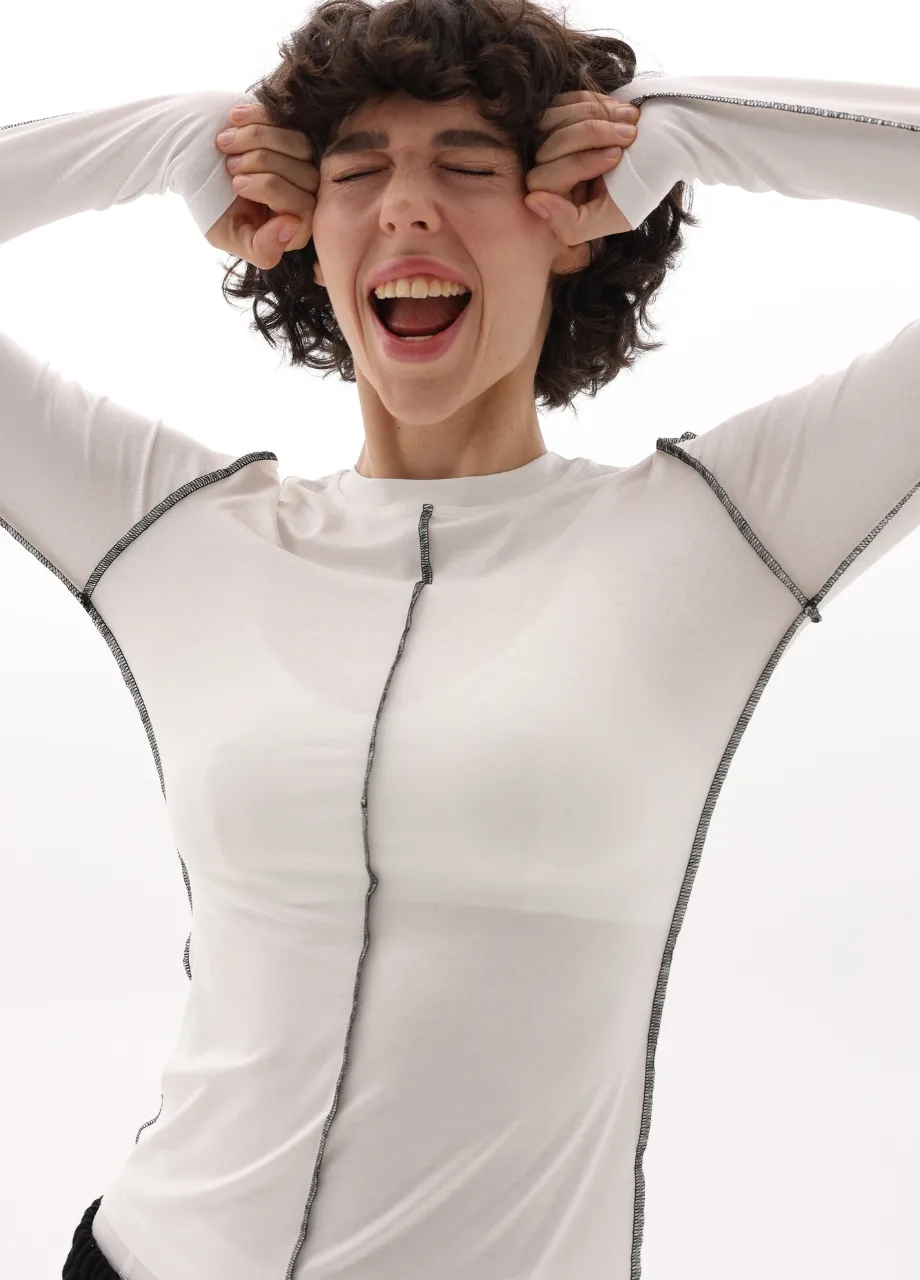 14 › Str/Cd Wear Person with hands pulling at sides of head, mouth open in a joyful scream, wearing a white top, conveying excitement and playfulness.