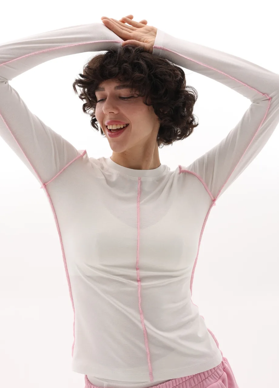 3 › Str/Cd Wear Smiling woman with short curly hair stretching arms overhead, wearing a white top with pink seams.
