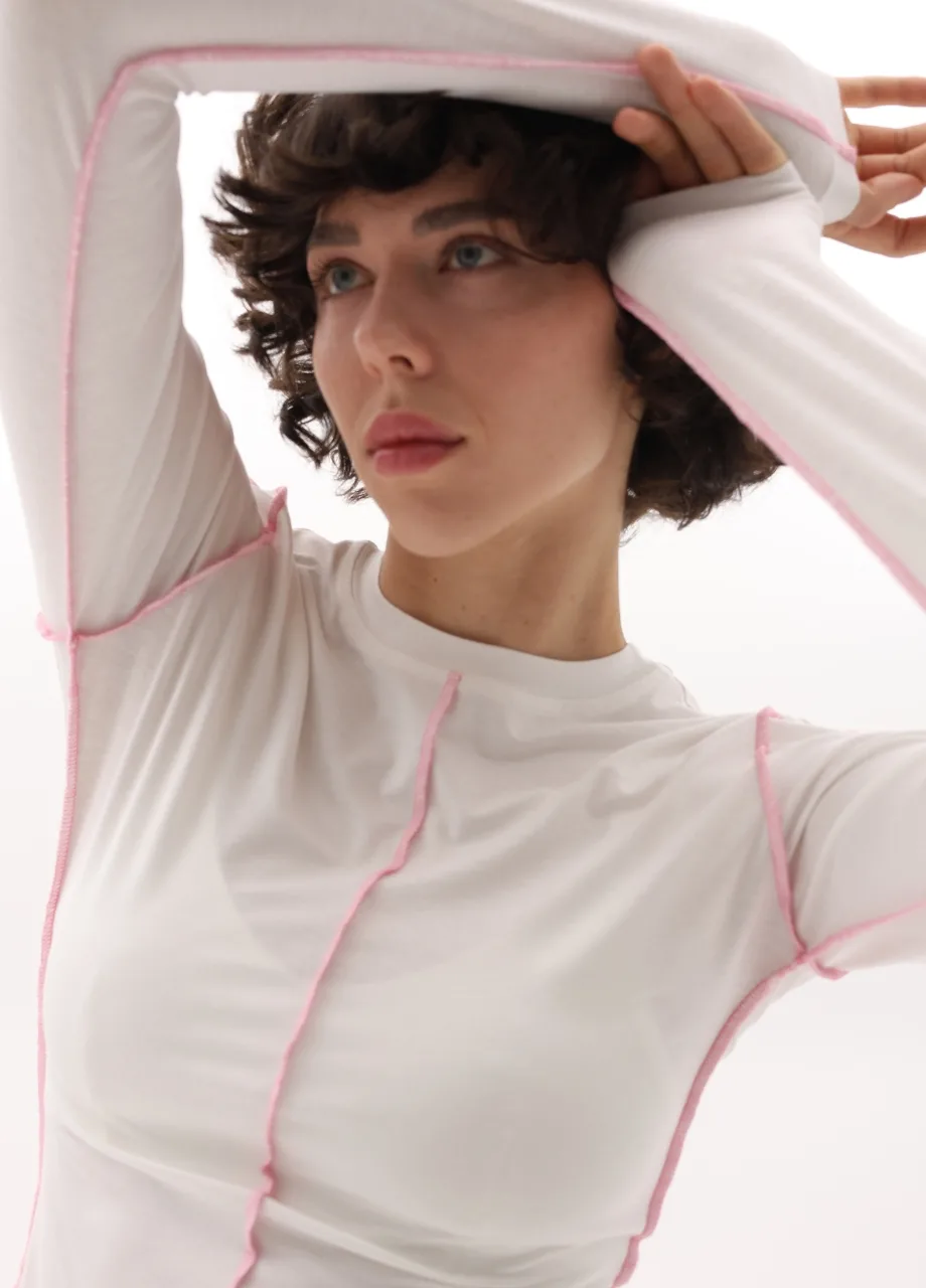 5 › Str/Cd Wear Person with short dark hair wearing a white top with pink seams, arms raised and looking off to the side.