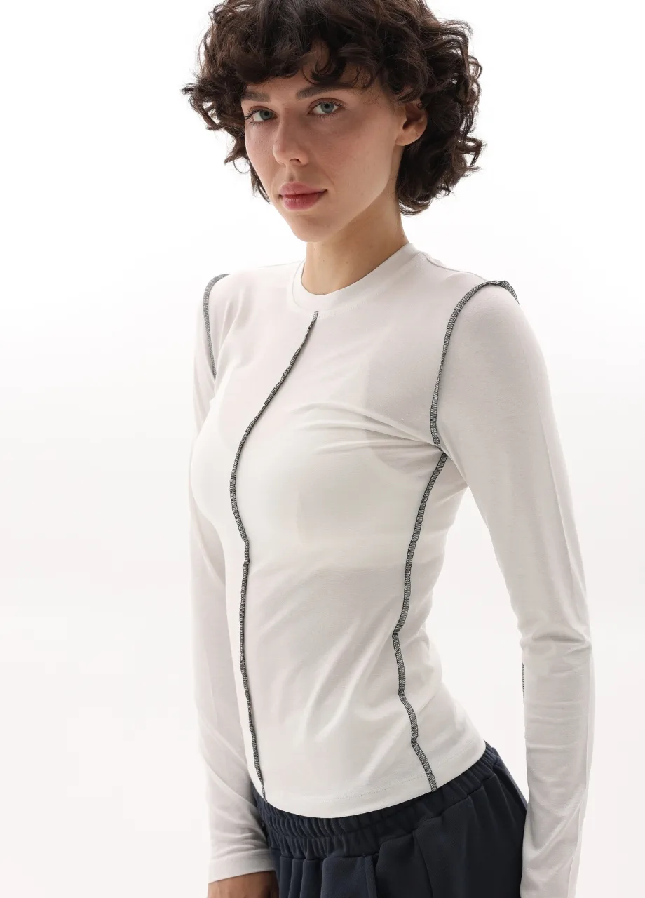 8 › Str/Cd Wear Female model wearing a white fitted long-sleeve top with black contrast seams, standing against a white background.