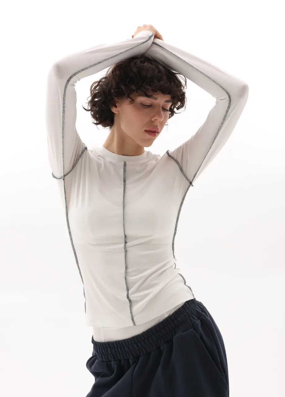 9 › Str/Cd Wear Person with short dark hair wearing a white long-sleeve top with visible seams, arms raised overhead, against a white background.